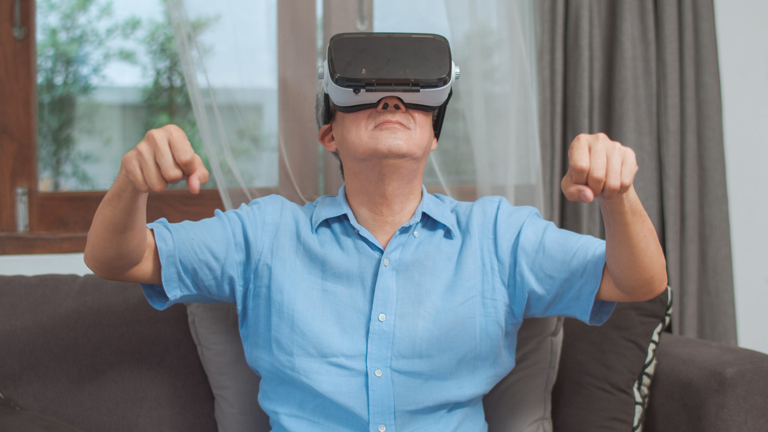 Asian senior men play games at home. Asian senior older Chinese male happy fun and virtual reality, VR playing games while lying sofa in living room at home concept.