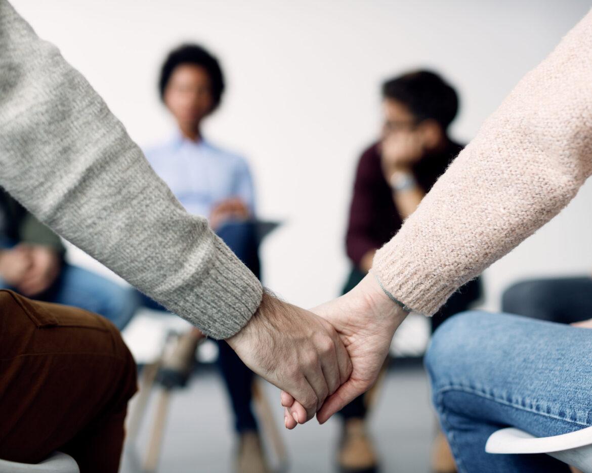 Close-up of two people holding hands during group therapy.