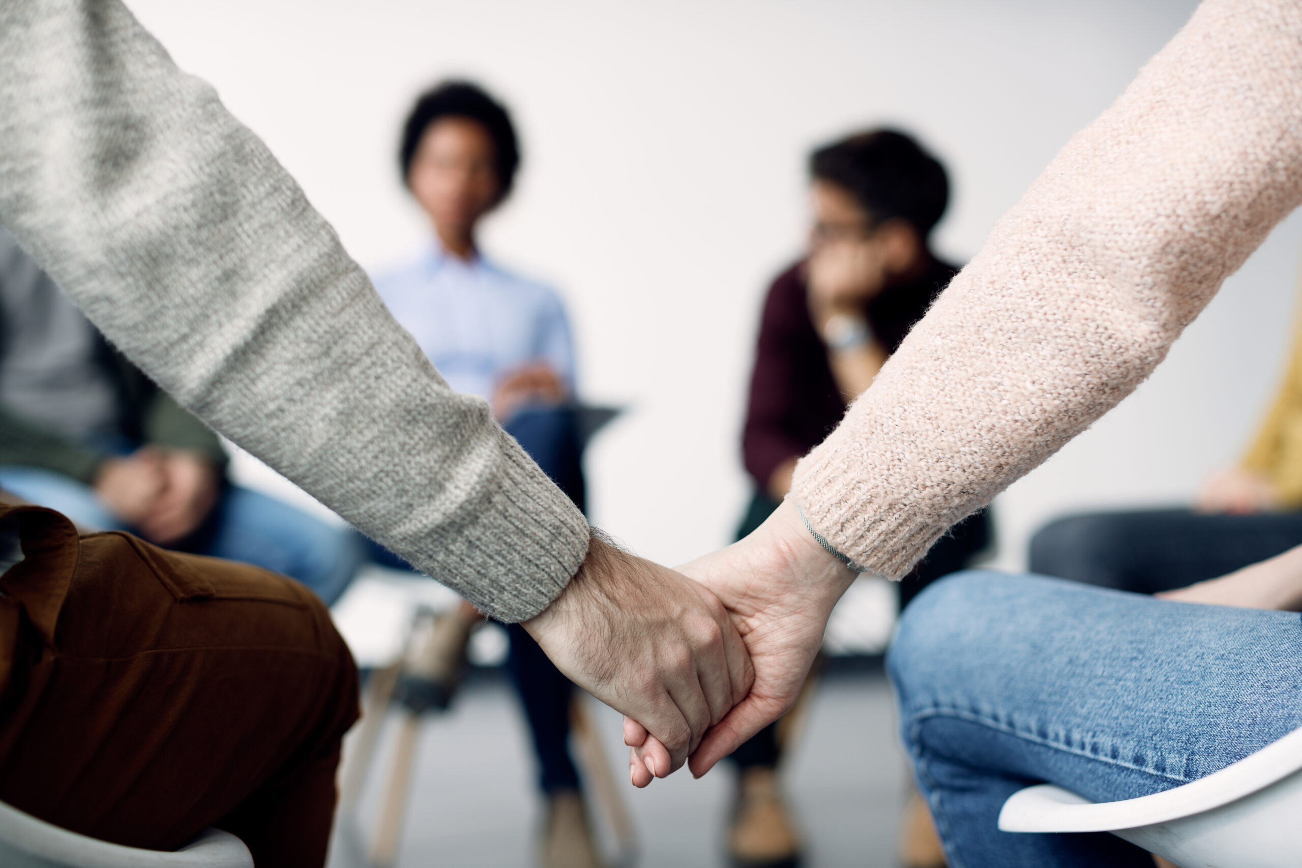 Close-up of two people holding hands during group therapy.