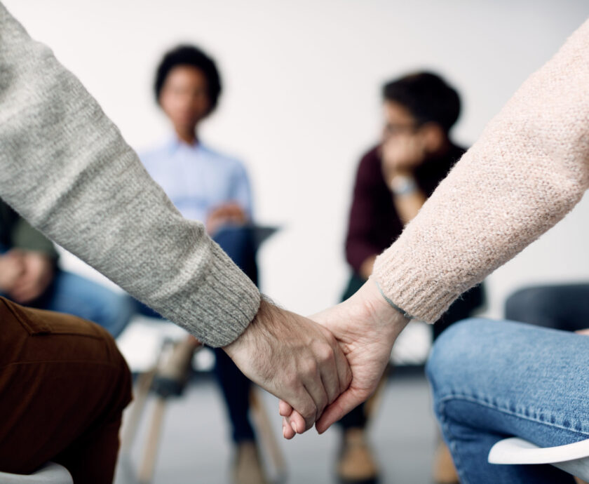 Close-up of two people holding hands during group therapy.