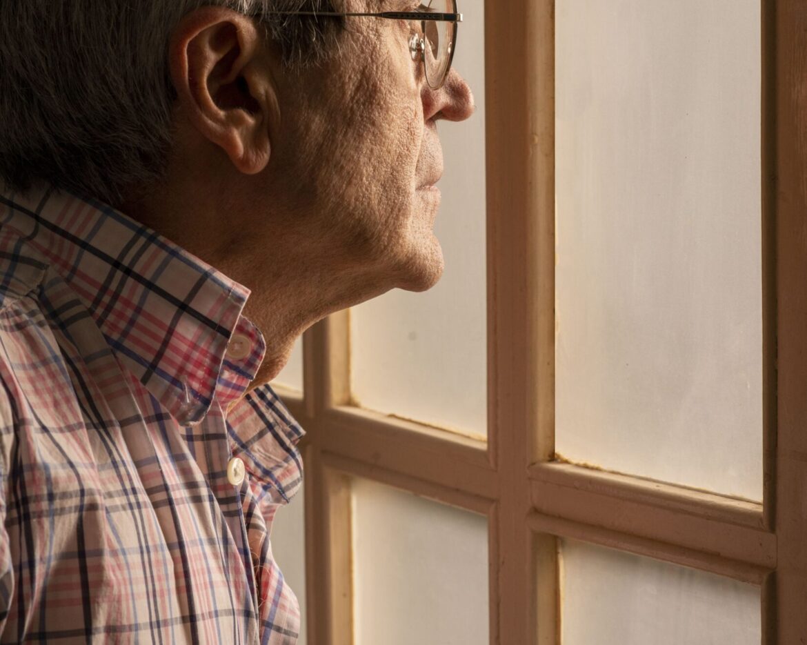 Vertical picture of an old man in glasses looking through the window